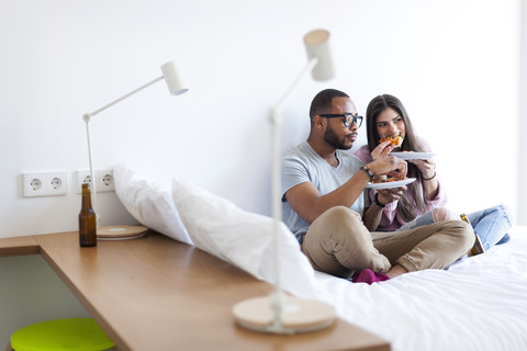 Junges Paar auf dem Bett, Pizza essen, lizenzfreies Stockfoto