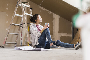 Young woman renovating her new home, holding construction plan - UUF10081