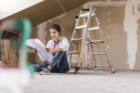 Junge Frau bei der Renovierung ihres neuen Hauses, mit Bauplan, lizenzfreies Stockfoto