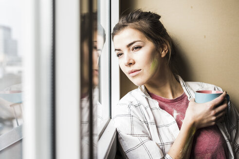Junge Frau hält Kaffeetasse und schaut aus dem Fenster - UUF10089