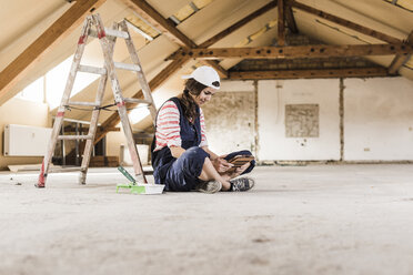 Junge Frau sitzt auf einer Baustelle und schaut auf ihr digitales Tablet - UUF10091