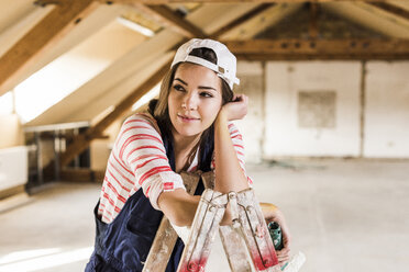 Junge Frau, die ihr neues Haus renoviert, hält eine Farbrolle - UUF10095