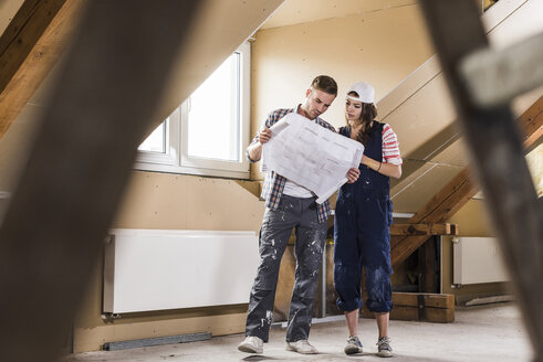 Young couple on construction site of their new home, looking at construction plan - UUF10103