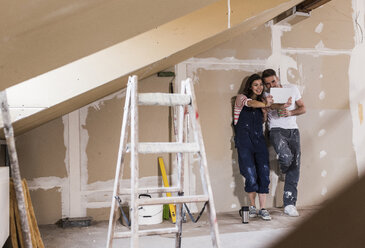 Young couple on construction site of their new home, using digital tablet - UUF10110