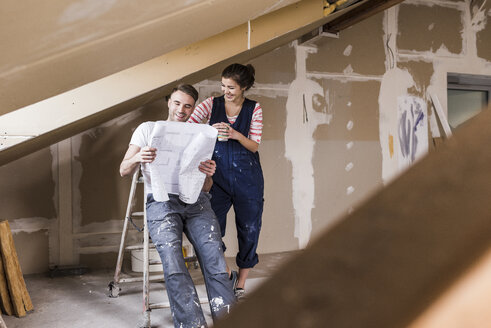 Junges Paar auf der Baustelle ihres neuen Hauses, Blick auf den Bauplan - UUF10111