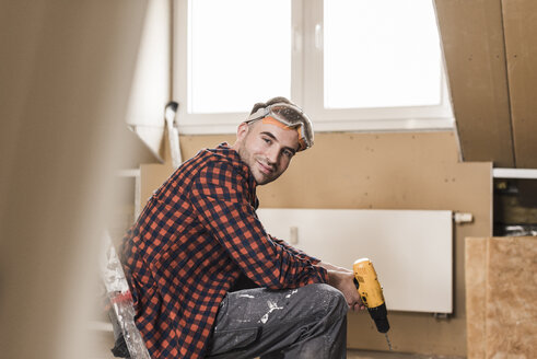 Yooung man renovating his new home, holding electric drill - UUF10114