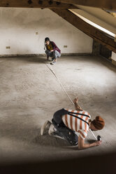 Young man and woman measuring floor on construction site - UUF10125