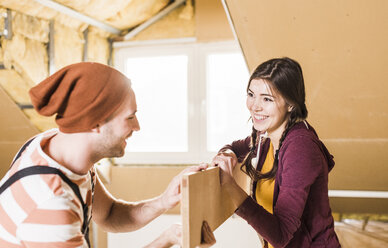 Young man and woman renovating their new home, holding a plank - UUF10132