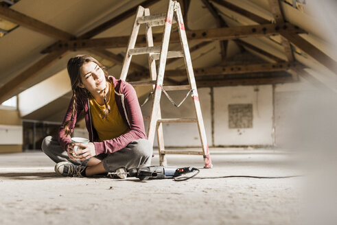Unabhängige junge Frau bei der Renovierung ihres neuen Hauses, auf dem Boden sitzend mit einer Tasse Kaffee - UUF10138
