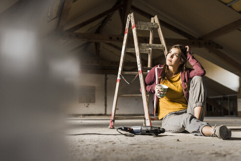 Unabhängige junge Frau bei der Renovierung ihres neuen Hauses, auf dem Boden sitzend mit einer Tasse Kaffee - UUF10139