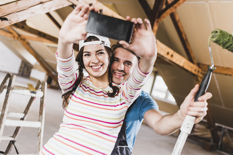 Junges Paar renoviert sein neues Haus und macht dabei Selfies mit dem Smartphone, lizenzfreies Stockfoto