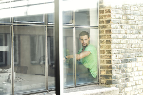 Junge Berufstätige, die am Fenster sitzen und besorgt aussehen, lizenzfreies Stockfoto