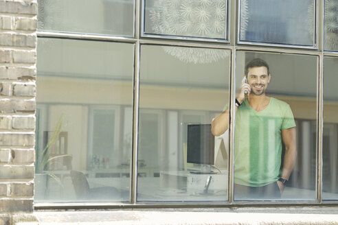 Junger Berufstätiger am Fenster, der selbstbewusst telefoniert - SBOF00301