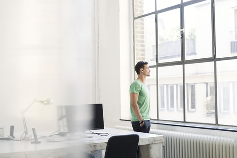 Junger Geschäftsmann schaut nachdenklich aus dem Bürofenster, lizenzfreies Stockfoto