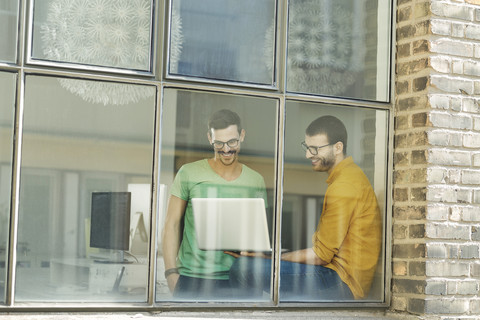 Junge Berufstätige am Fenster mit Laptop, lizenzfreies Stockfoto