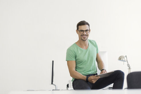 Junger Geschäftsmann im Büro sitzt auf dem Schreibtisch mit digitalem Tablet - SBOF00316