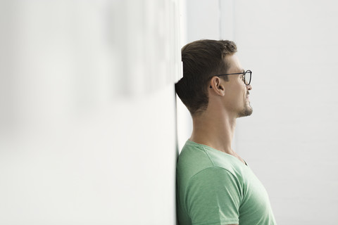 Junger Geschäftsmann im Büro an die Wand gelehnt, lizenzfreies Stockfoto