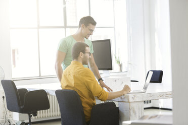 Two businessmen working together in office, using laptop - SBOF00320