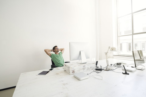 Junger Geschäftsmann im Büro entspannt am Schreibtisch, lizenzfreies Stockfoto