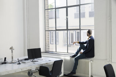 Young businessman looking out of office window - SBOF00327