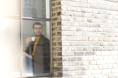 Geschäftsmann sitzt auf der Fensterbank und trinkt Kaffee - SBOF00330