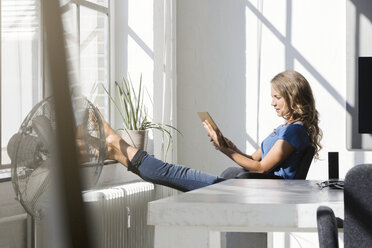 Casual businesswoman in office using digtal tabet with feet on window sill - SBOF00338