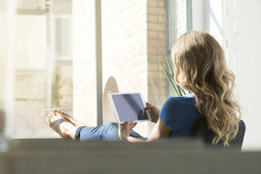 Casual businesswoman in office using digtal tabet with feet on window sill - SBOF00339