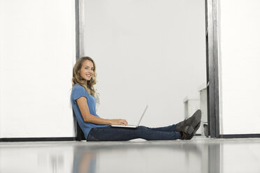 Lässige Geschäftsfrau im Büro, die auf dem Boden sitzt und einen Laptop benutzt - SBOF00349