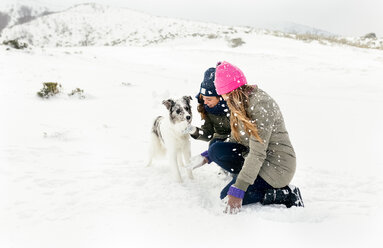 Zwei Freunde spielen mit einem Hund im Schnee - MGOF03027