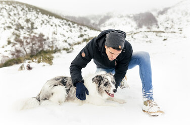 Junger Mann streichelt seinen Hund im Schnee - MGOF03033