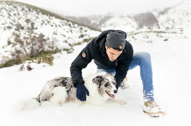 Young man stroking his dog in the snow - MGOF03033