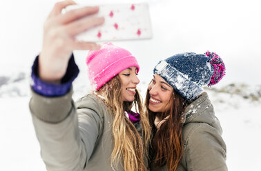 Two friends taking smart phone selfies in the snow - MGOF03057