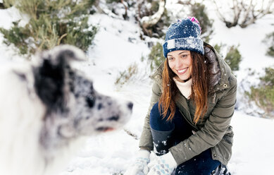 Schöne Frau spielt mit ihrem Hund im Schnee - MGOF03064