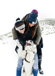 Junges Paar spielt mit seinem Hund im Schnee - MGOF03074