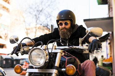 Porträt eines bärtigen Motorradfahrers mit Helm und Sonnenbrille, der auf seinem Motorrad sitzt - KKAF00495