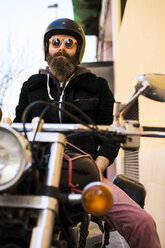 Porträt eines bärtigen Motorradfahrers mit Helm und Sonnenbrille, der auf seinem Motorrad sitzt - KKAF00496