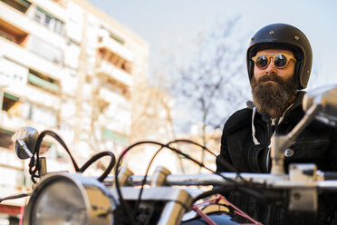 Porträt eines bärtigen Motorradfahrers mit Helm und Sonnenbrille, der auf seinem Motorrad sitzt - KKAF00497