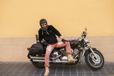 Portrait of bearded biker wearing helmet and sunglasses sitting on his motorcycle - KKAF00498