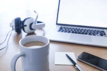 Cup of coffee, headset, smartphone, ballpen, adhesive note and laptop on desk - TCF05312