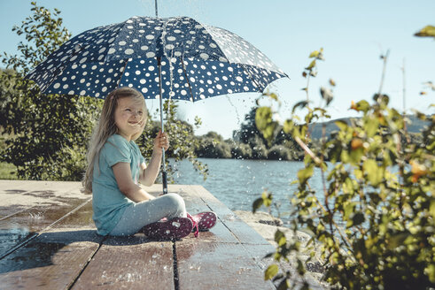 Mädchen mit Regenschirm sitzt auf einem Steg am See, während Wassertropfen auf sie herabfallen - IPF00366