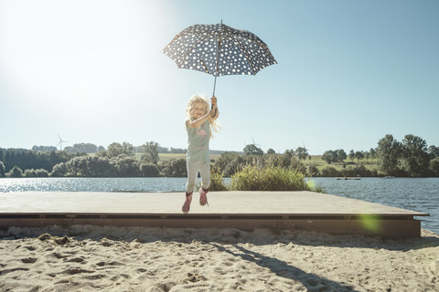 Mädchen mit Regenschirm springt an einem sonnigen Tag von einem Steg, lizenzfreies Stockfoto