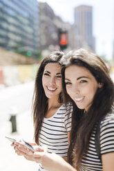 USA, New York City, two happy twin sisters with cell phones in Manhattan - GIOF02180