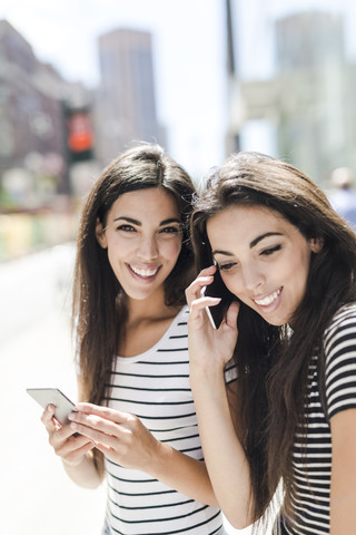 USA, New York City, two happy twin sisters with cell phones in Manhattan stock photo