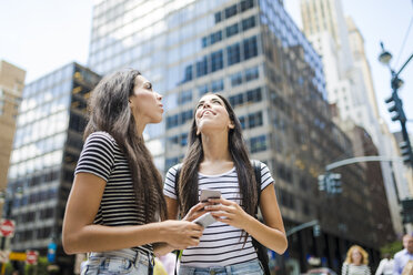 USA, New York City, two twin sisters with cell phones in Manhattan looking up - GIOF02185