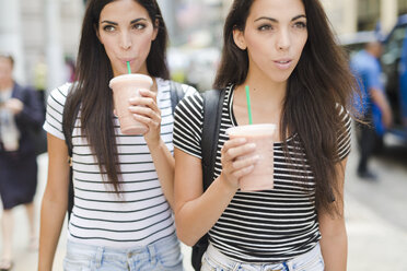 USA, New York City, two twin sisters on the go in Manhattan with takeaway drink - GIOF02195