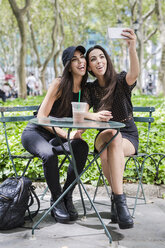 Zwei Zwillingsschwestern machen ein Selfie am Tisch in einem Park - GIOF02211