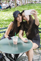 Zwei Zwillingsschwestern machen ein Selfie am Tisch in einem Park - GIOF02212