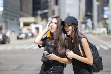 USA, New York City, two happy twin sisters with cell phones in Manhattan - GIOF02220