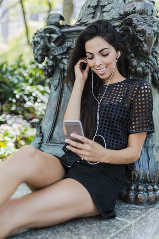 Lächelnde brünette junge Frau hört Musik mit Ohrstöpseln, lizenzfreies Stockfoto