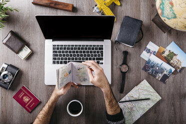 Overhead view of man's hand holding passport and travel items on table - JRFF01247